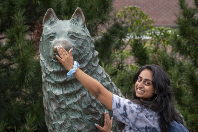 smiling student rubbing the nose on the Jonathan the husky statue